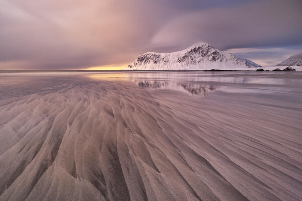 a warm light envelope the iconic mountainn in front at Skagsanden beach during a winter sunset, Ramberg, Lofoten island, Norway, Europe