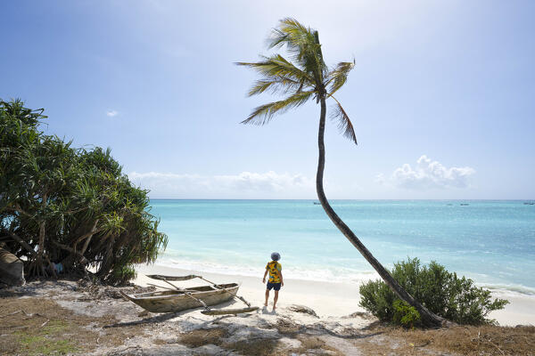 a tourist admiring the beach during a beautiful sunny day, near a coconut palm and fisherman boat, Zanzibar, Tanzania, Africa