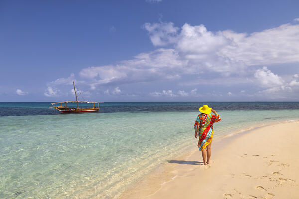 one tourist walking on the beach during a sunny day with a dhow in foreground, Zanzibar, Tanzania, Africa