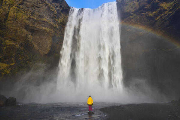 a girl observe the majestic Skogafoss waterfall witha a rainbow, during an autumn day, Iceland, Europe