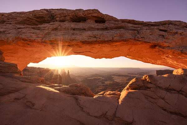 the sunlight envelope the Canyonlands valley during a summer sunrise, framed by Mesa Arch, Utah, United States of America