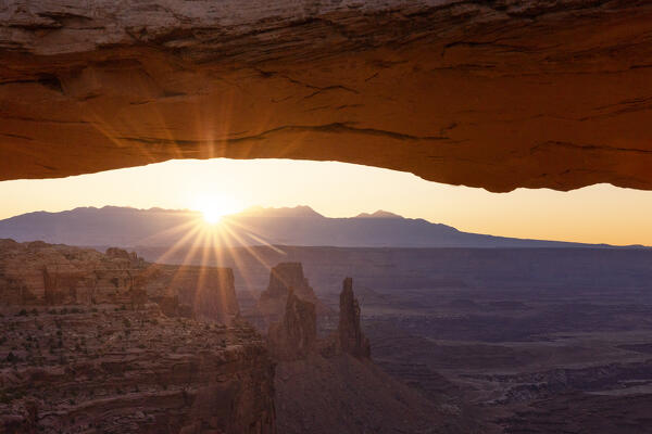 the sunlight envelope the Canyonlands valley during a summer sunrise, framed by Mesa Arch, Utah, United States of America