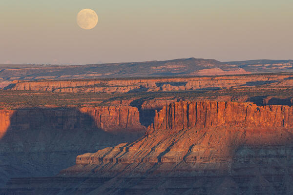 the sunlight envelope the Canyonlands valley during a summer sunset with a moonrise, Utah, United States of America
