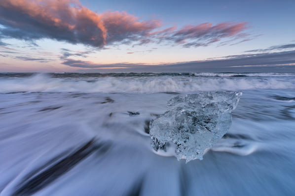Little block of ice on the black beach at sunset in Jokulsarlon Glacier Lagoon, Austurland, Eastern Iceland, Iceland, Europe