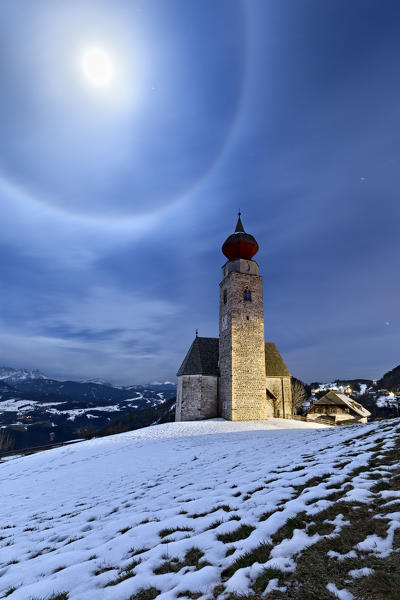 The medieval church of San Nicolò in Monte di Mezzo with the lunar halo. Renon plateau, Bolzano province, Trentino Alto-Adige, Italy, Europe.