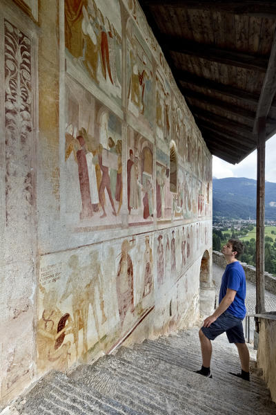 Man looks at the paintings of Simone II Baschenis on the facade of the Santo Stefano church in Carisolo. Rendena Valley, Trento province, Trentino Alto-Adige, Italy, Europe.