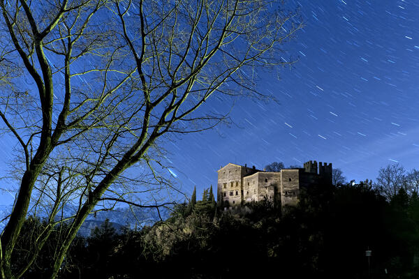 Skeletal trees frame Madruzzo Castle on a spooky night. Madruzzo, Trento province, Trentino Alto-Adige, Italy, Europe.