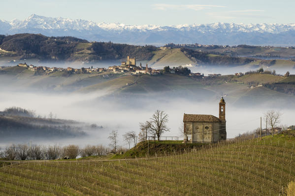 Vineyards in Langhe with a chapel on the foreground, Serralunga D'Alba on the middleground and Alps Chain on the background during a foggy day,Montelupo Albese,Piedmont, Italy