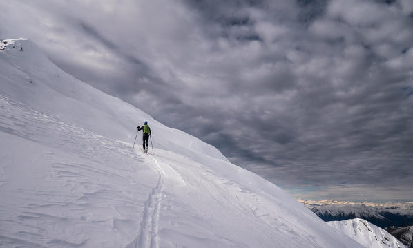 A ray of light and a man skiing uphill at Melasc peak, Valgerola, Valtellina, Italy, Alps