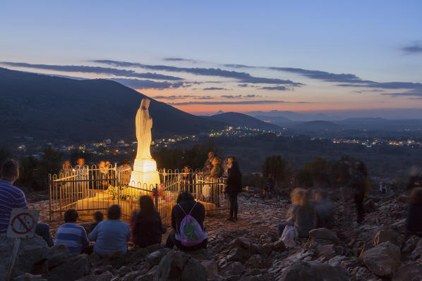 Europe, Balkans, Bosnia and Herzegovina, Medjugorje. Pilgrims praying near the statue of the Virgin Mary on the apparition hill