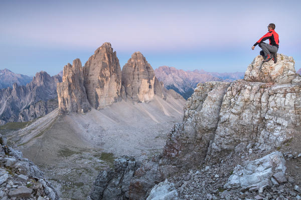 Hiker on the top of mount Paterno / Paternkofel looking the sunrise towards Tre Cime di Lavaredo, Sexten Dolomites, South Tyrol, Bolzano, Italy