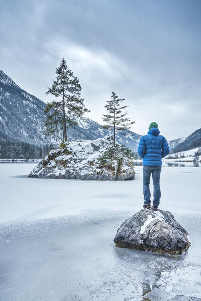 A man looking the little rocky island at the Hintersee lake in winter, Hintersee, Berchtesgaden, Bavaria, Germany