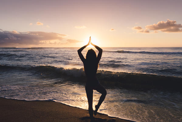 A girl doing yoga positions during sunrise in Kapaa beach park, Kauai islands, Hawaii, USA