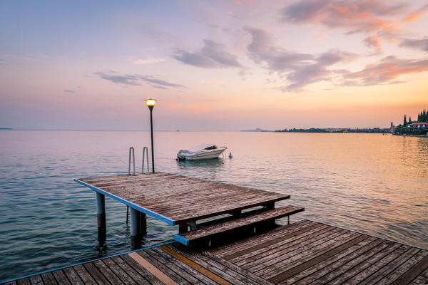 A pier on the western side of Garda Lake, near Toscolano Maderno, during a colored sunset. Toscolano Maderno, Brescia Province, Garda Lake, Italy.