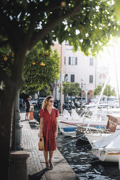 Blonde girl with red dress walking in Gargnano, a small village on Garda Lake, Brescia province, Lombardy, Italy