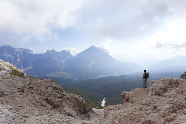 A hiker admires the landscape from Sentiero Flaibani (Flaibani trail) towards Borca and San Vito di Cadore, Pelmo group, Dolomites, Belluno province, Veneto, Italy.