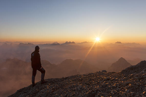 A hiker admires the sunrise at Punta Penia, Marmolada group, Dolomites, Canazei, Trento province, Trentino-Alto Adige, Italy