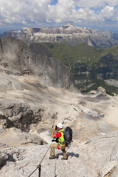 A mountaineer admires the Sella group from the Via Ferrata of West Ridge, Marmolada group, Dolomites, Canazei, Trento province, Trentino-Alto Adige, Italy