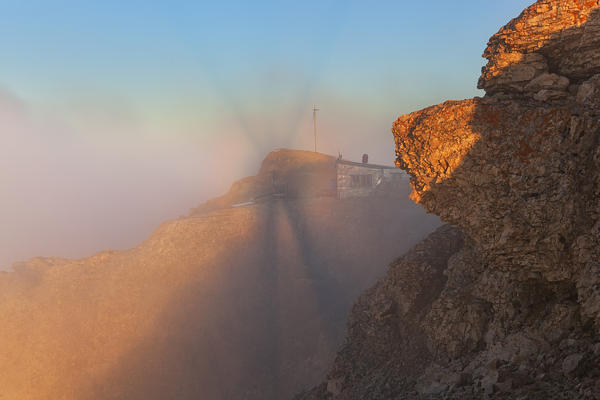 Brocken Spectrum on Punta Penia hut at dawn, Marmolada group, Dolomites, Canazei, Trento province, Trentino-Alto Adige, Italy