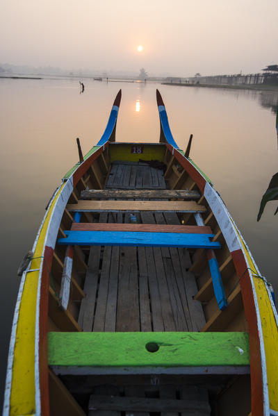 Amarapura, Mandalay region, Myanmar. Colorful boats moored on the banks of the Taungthaman lake  at sunrise, with the U Bein bridge in the background.