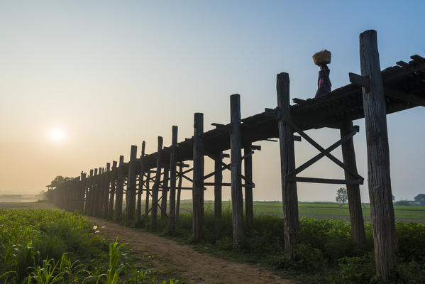 Amarapura, Mandalay region, Myanmar. Woman with basket on her head walking on the U-Bein bridge at sunrise.