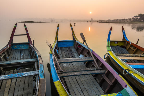 Amarapura, Mandalay region, Myanmar. Colorful boats moored on the banks of the Taungthaman lake  at sunrise, with the U Bein bridge in the background.