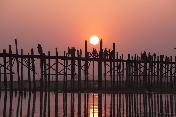 Amarapura, Mandalay region, Myanmar. Silhouetted people walking on the U Bein bridge at sunset.