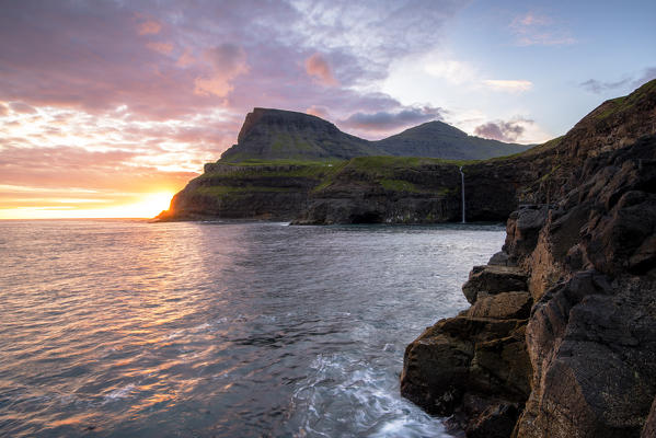 Gasadalur, Vagar island, Faroe Islands, Denmark. The iconic waterfall jumping from the cliff into the ocean at sunset.