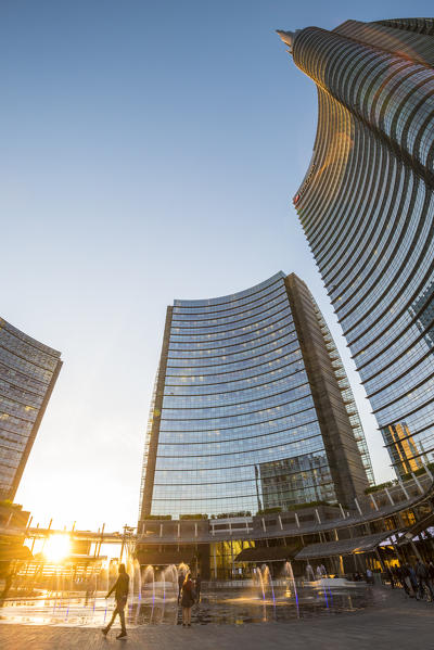 Milan, Lombardy, Italy. People walking in Gae Aulenti square in the Porta Nuova business district at sunset.