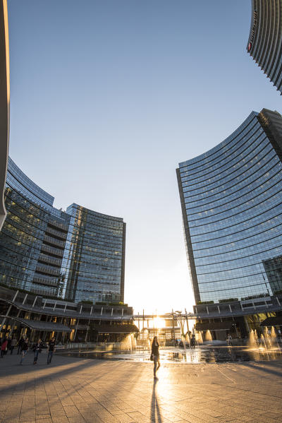 Milan, Lombardy, Italy. People walking in Gae Aulenti square in the Porta Nuova business district at sunset.