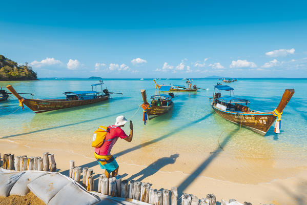 Ao Lo Bakao (Lo Bakao Bay), Ko Phi Phi Don, Krabi Province, Thailand. Tourist photographing moored traditional longtail boats.