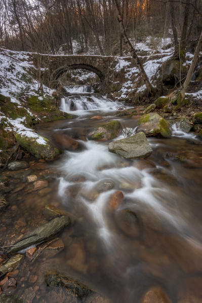 Cuasso al Monte, Varese, Lombardy, Italy. An old roamn bridge with snow and little waterfalls.