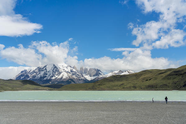 Two people on the shore of Laguna Amarga, with Paine Towers in the background, in summer. Torres del Paine National Park, Ultima Esperanza province, Magallanes region, Chile.
