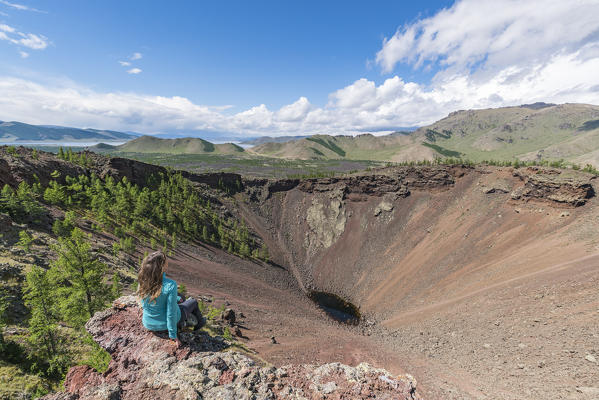 Woman sitting over Khorgo volcano crater and White Lake in the background. Tariat district, North Hangay province, Mongolia.