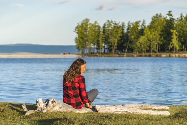 Woman with long hair and checked shirt sitting on a log on the shores of Hovsgol Lake. Hovsgol province, Mongolia.