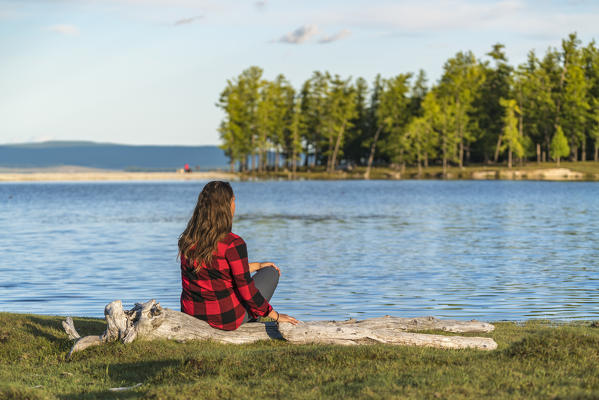 Woman with long hair and checked shirt sitting on a log on the shores of Hovsgol Lake. Hovsgol province, Mongolia.