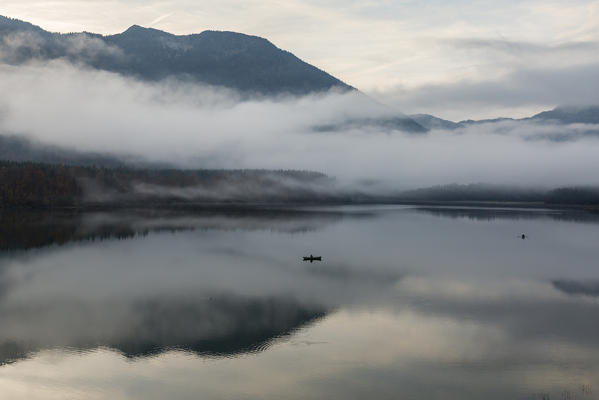 One fishing boat in the middle of Sylvenstein lake in the morning mist. Bad Tölz-Wolfratshausen district, Bavaria, Germany.
