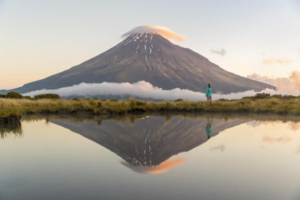 Woman staring at Mount Taranaki at sunset. Egmont National Park, New Plymouth district, Taranaki region, North Island, New Zealand.