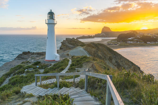 People watching the sun setting down behind Castle Rock and Castlepoint lighthouse.  Castlepoint, Wairarapa region, North Island, New Zealand.