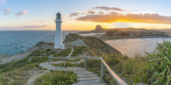 People watching the sun setting down behind Castle Rock and Castlepoint lighthouse.  Castlepoint, Wairarapa region, North Island, New Zealand.