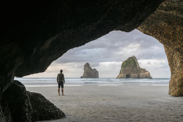 Man staring at two of the Archway Islands. Wharariki beach, Puponga, Tasman district, South Island, New Zealand.