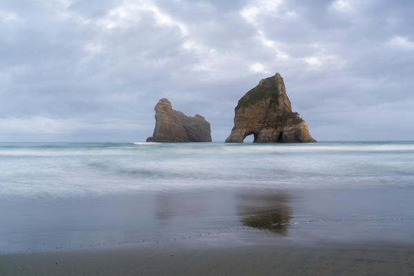 Moody sky above two of the Archway Islands. Wharariki beach, Puponga, Tasman district, South Island, New Zealand.
