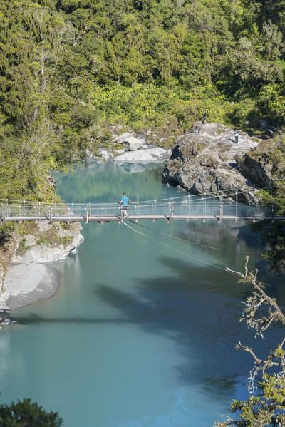 Man walking on a boardwalk over Hokitika river. Hokitika, West Coast region, South Island, New Zealand.