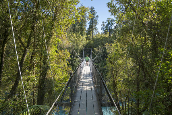 Young woman walking on a boardwalk over Hokitika river. Hokitika, West Coast region, South Island, New Zealand. (MR)