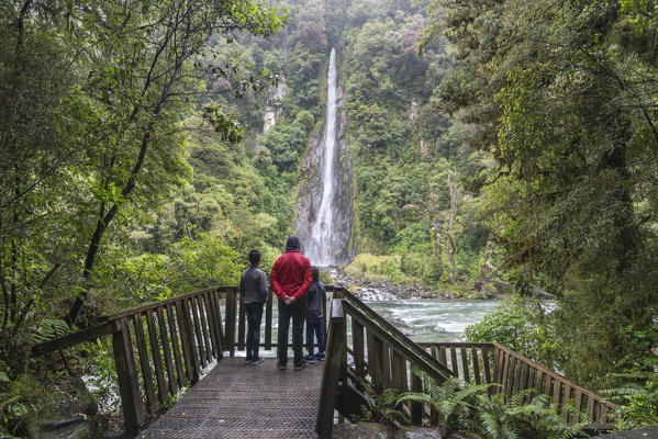 Tourists under the rain admiring Thunder Creek Falls. Mount Aspiring National Park, West Coast region, South Island, New Zealand.