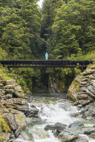 Person standing on a bridge over a creek near Haast Pass. Mount Aspiring National Park, West Coast region, South Island, New Zealand.