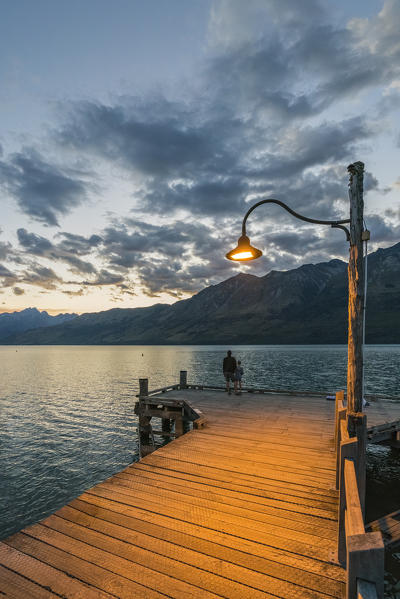 Man and child on the jetty at dusk. Glenorchy, Queenstown Lake district, Otago region, South Island, New Zealand.