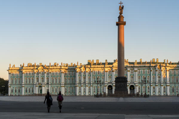 Two people walking towards Winter Palace and Alexander column on Palace Square. Saint Petersburg, Russia.