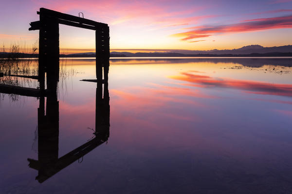 Monte Rosa and the remaining of an old boathouse reflecting on Lake Varese during a winter sunset at Calcinate del Pesce, Varese Province, Lombardy, Italy.