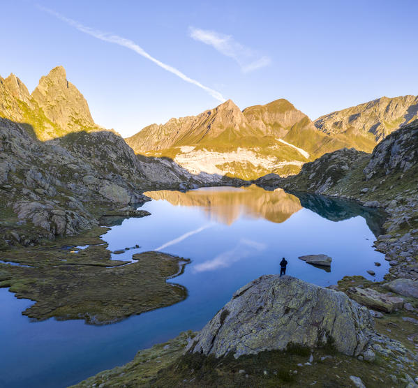 A lonely man admiring a sunrise at Lago Leit with Pizzo Prevat reflecting on it. Rodi, Prato Leventina, Valle Leventina, Canton Ticino, Switzerland.